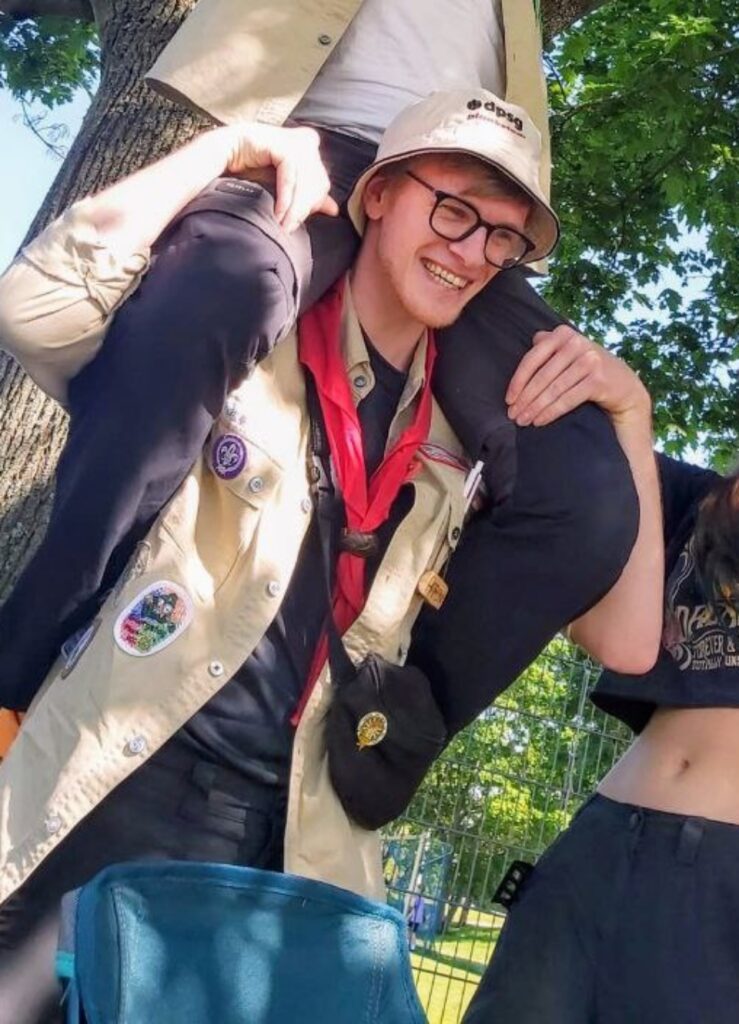 Aaron in Pfadfinderkluft. Er grinst. Jemand sitzt auf seinen Schultern